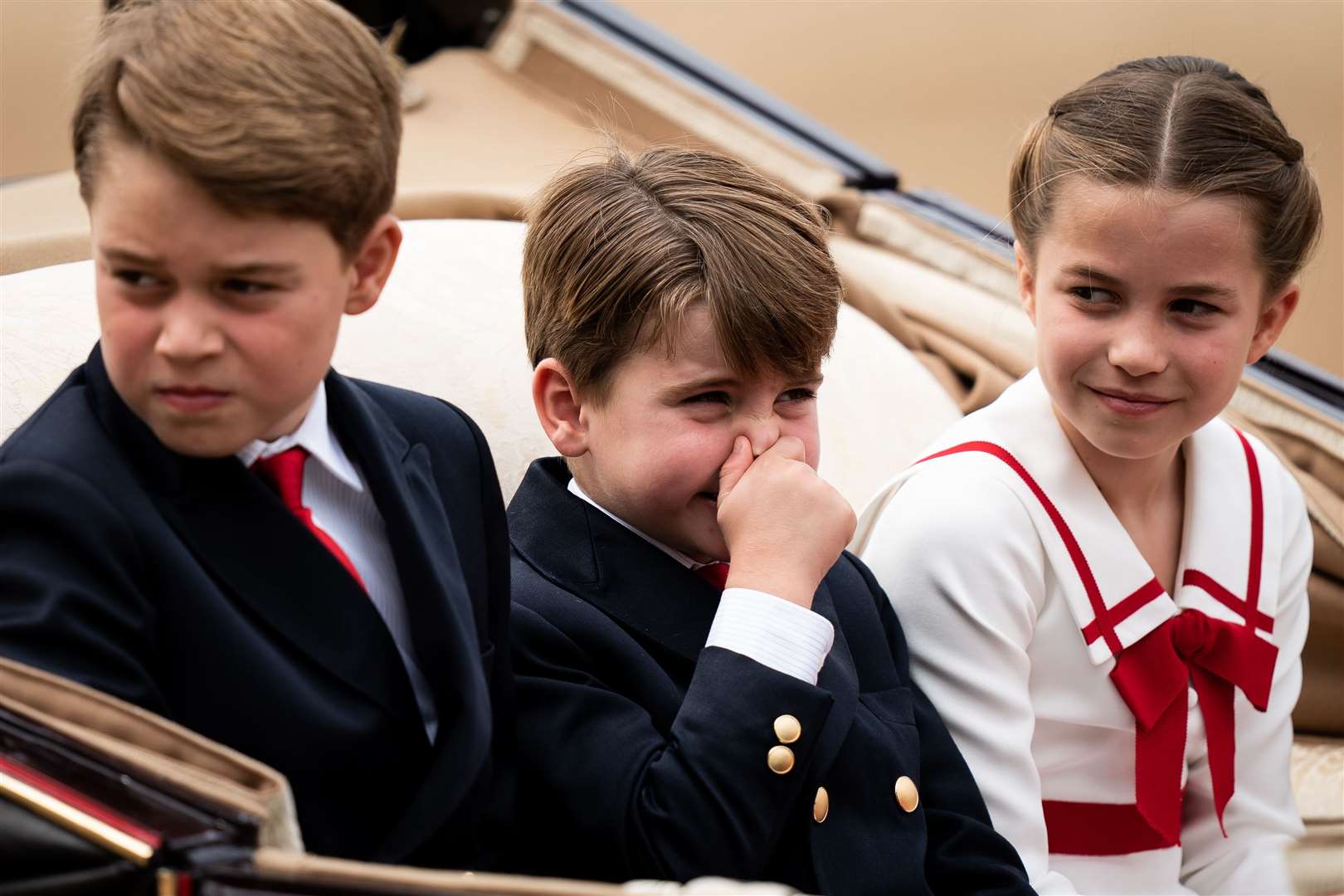 Louis holds his nose as he travels with George (left) and Charlotte in a carriage during the Trooping the Colour ceremony (Aaron Chown/PA)