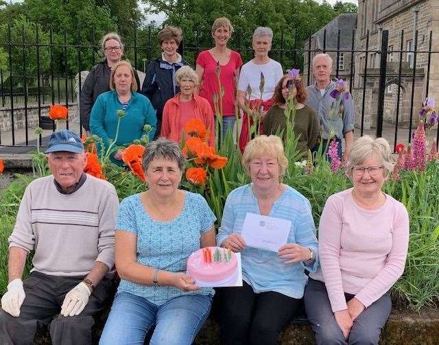 Forres In Bloom volunteers including Diane McGregor (holding cake) and Sandra Maclennan (holding letter) celebrating recognition from Her Majesty the Queen for their hard work.
