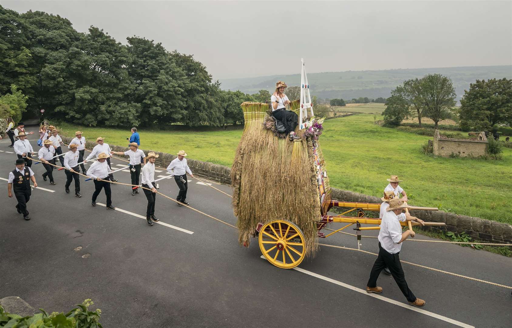 Men dressed in Panama hats, white shirts and clogs pull a 16ft-high thatched rush cart carrying a woman on top, during the Sowerby Bridge Rushbearing Festival in West Yorkshire (Danny Lawson/PA)