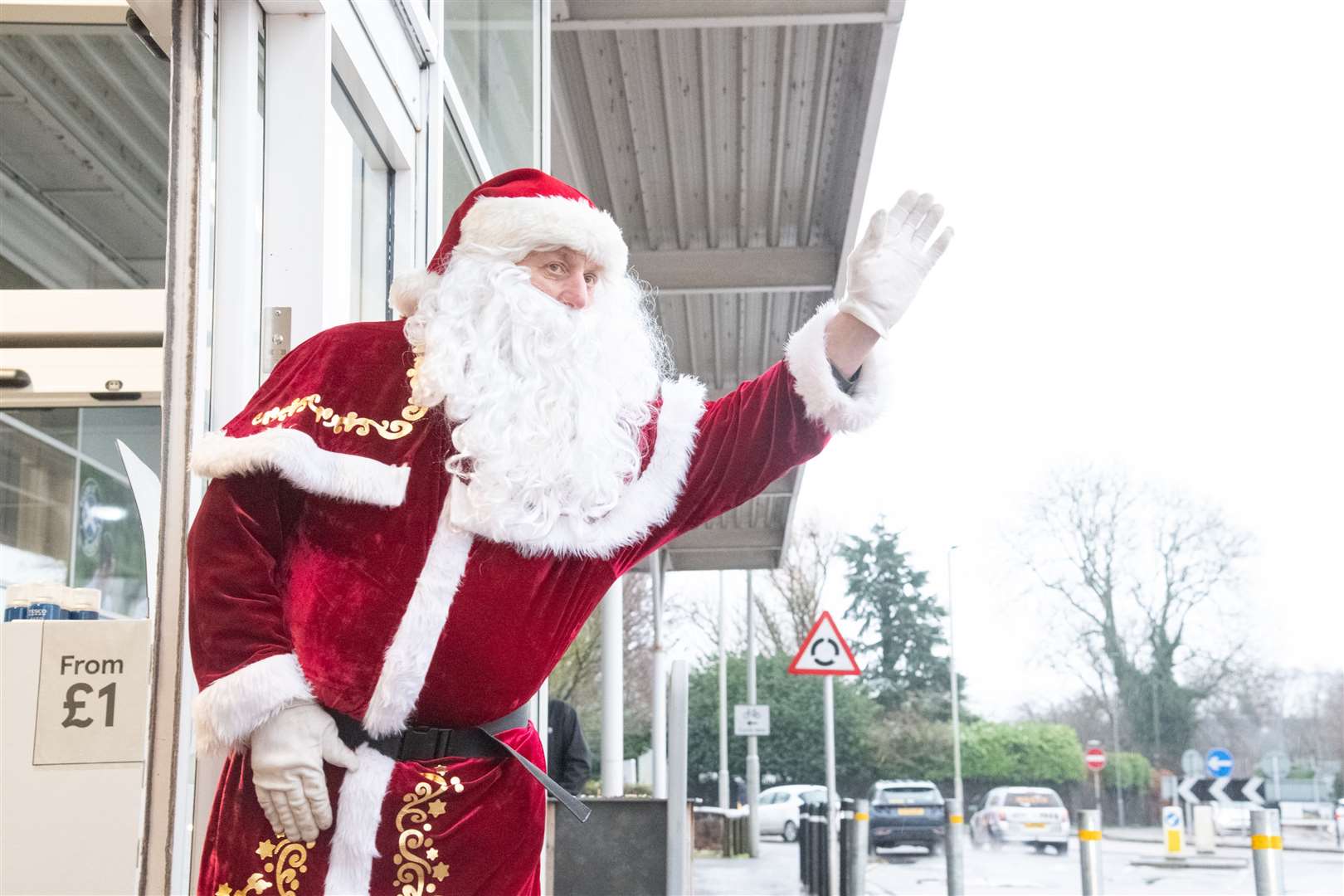 Santa waving to shoppers arriving in their cars.