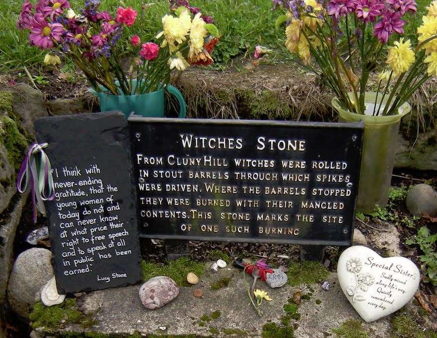 The stone and sign surrounded by tributes to the women who were executed due to prejudice.