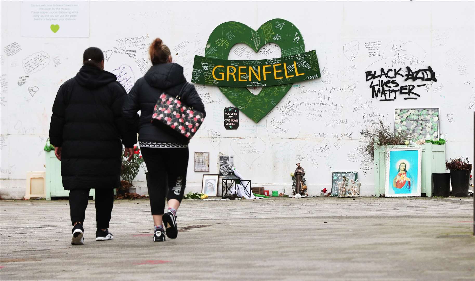 Two women walk towards the Grenfell Memorial Wall in the grounds of Kensington Aldridge Academy (Jonathan Brady/PA)