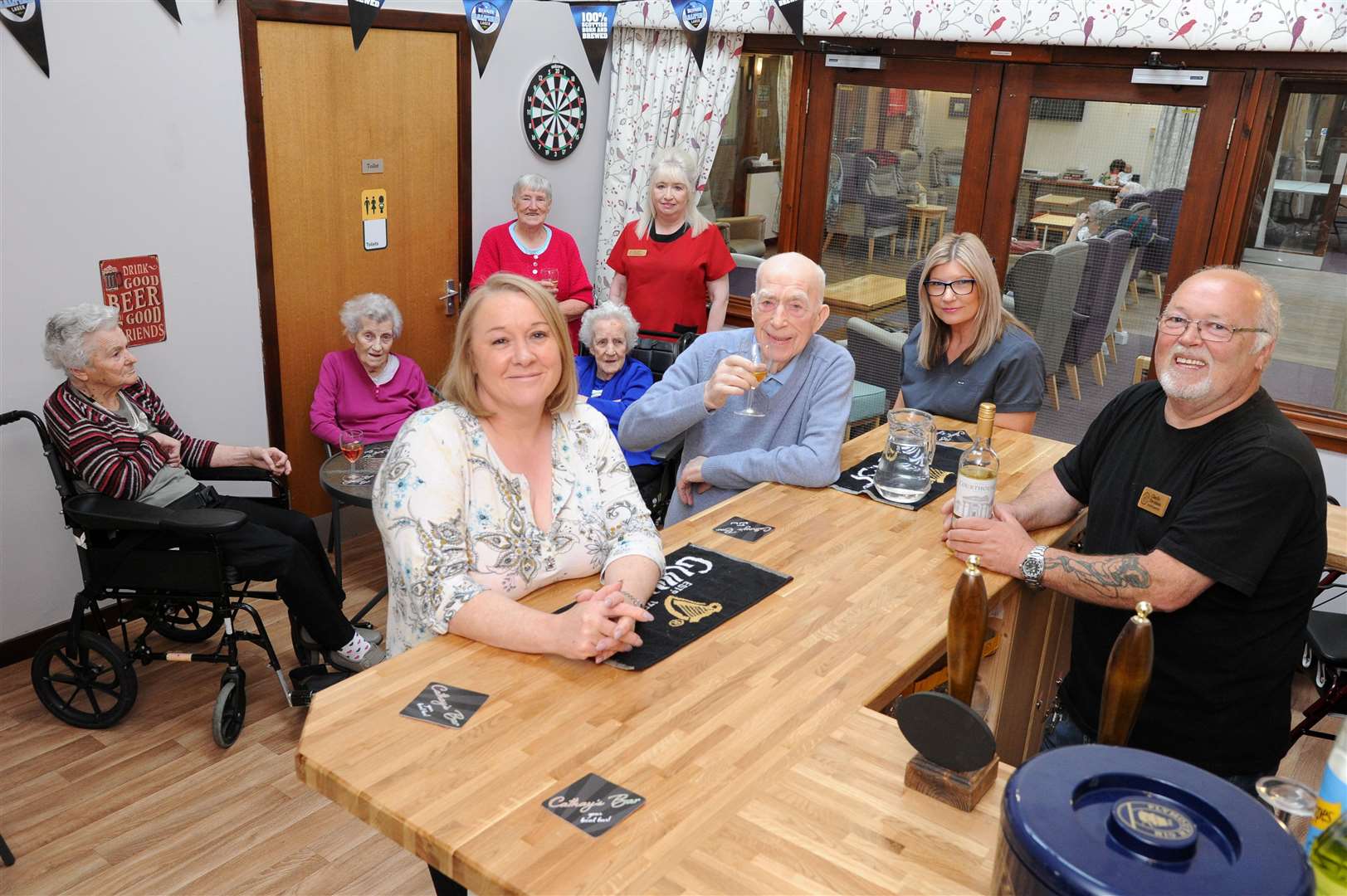 Cathay free bar manageress Elaine Crawford with 91-year-old resident George Garroee. Maintenance man Charlie Davidson (right) serves the drinks while activity co-ordinator Beverley Crawford (third centre) and other patrons wait.