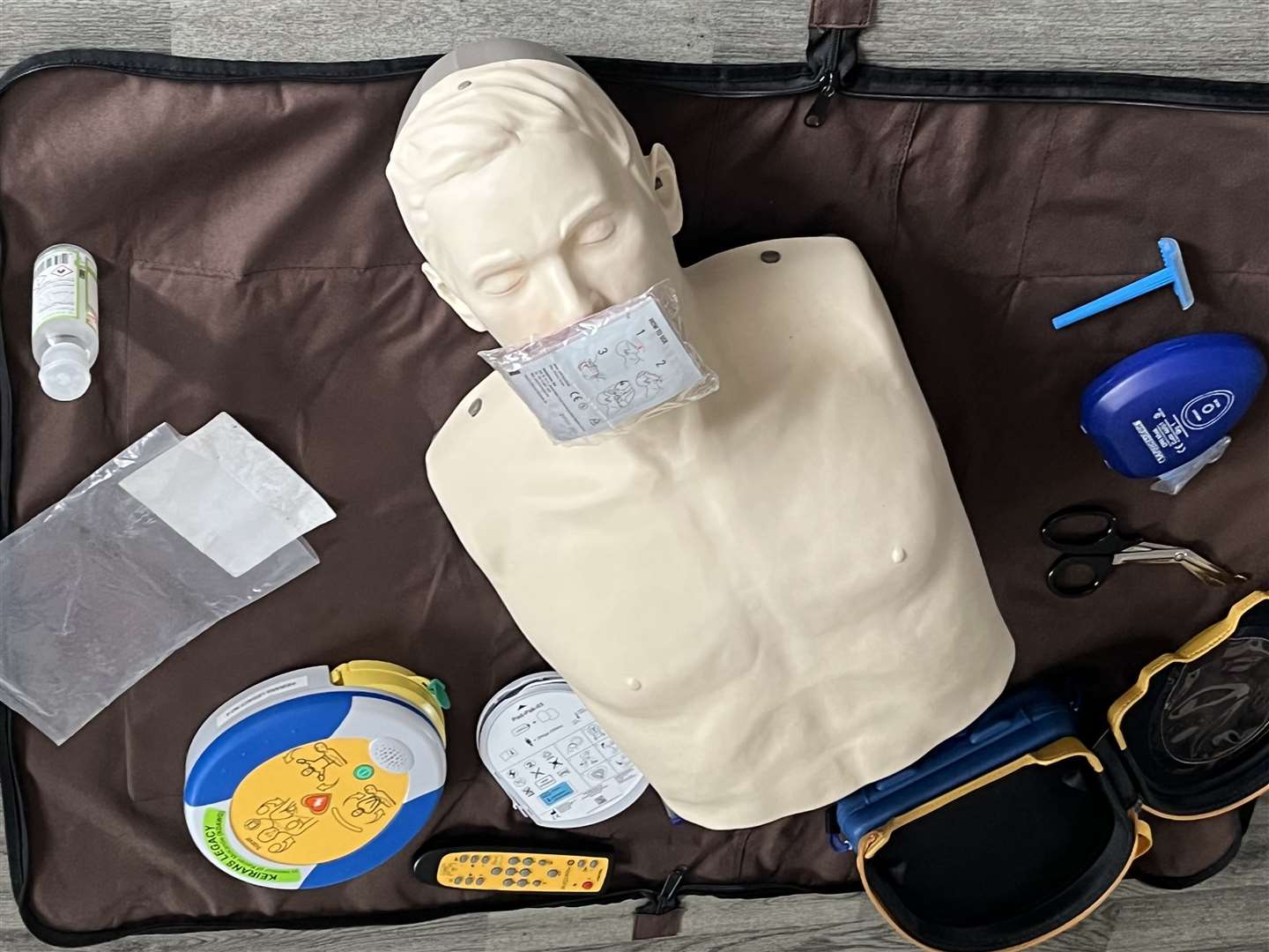 The contents of the defibrillator casing include the defib', child and adult pads, a mouth shield for mouth-to-mouth resuscitation, a razor in case shaving is required, and a pair of scissors to cut clothing.