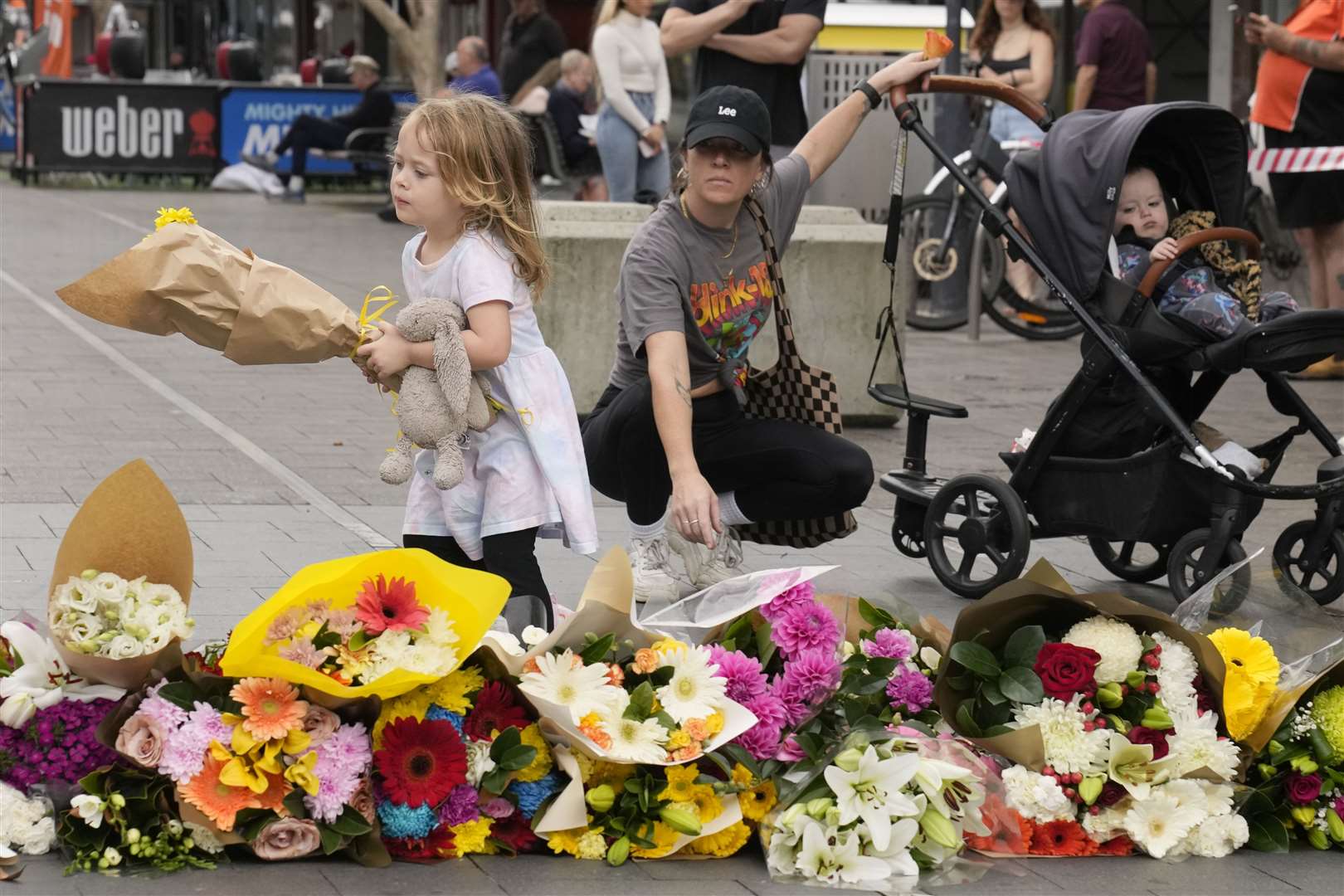 A young child carries flowers to place as a tribute near the crime scene at Bondi Junction (Rick Rycroft/AP)